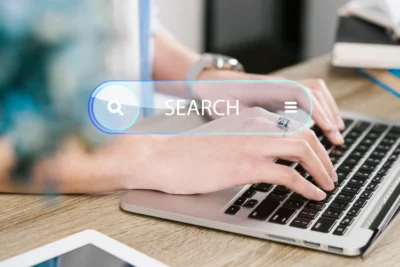 Imagem mostrando como os motores de busca realizam a pesquisa e indexação de sites. Um usuário digitando em um laptop com barra de pesquisa visível.
