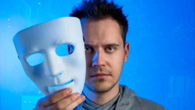 Homem segurando uma máscara de teatro representando uma ameaça de golpes com deepfakes e vozes falsas na era da inteligência artificial.